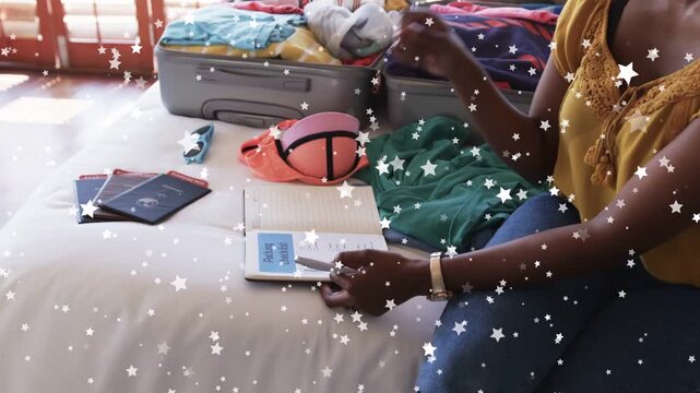 Woman sitting on bed resting hand on booklet, picking pen, writing, packing with star overlay