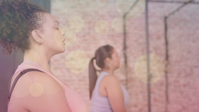 Two women on cue meditating in fitness, breathing for calm while bokeh intensifying around them