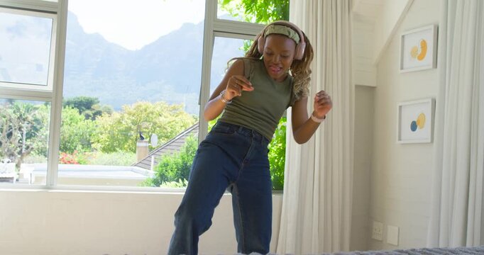 African woman dancing to music on headphones in bedroom, checking bracelets and adjusting headband