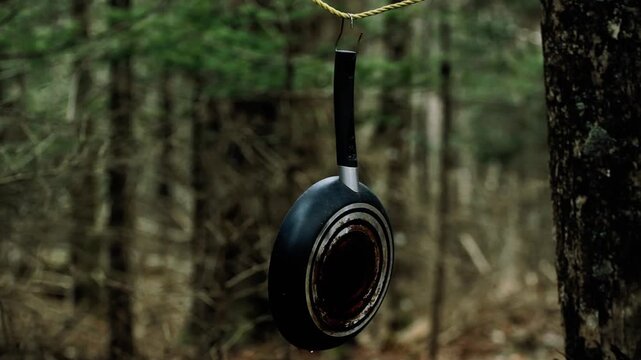 Rustic frying pan hanging from a rope in the forest. Camping and outdoor concept.