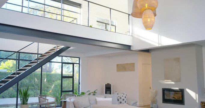 Camera is tilting down, revealing metal staircase and tall glass wall in mezzanine, exposing garden