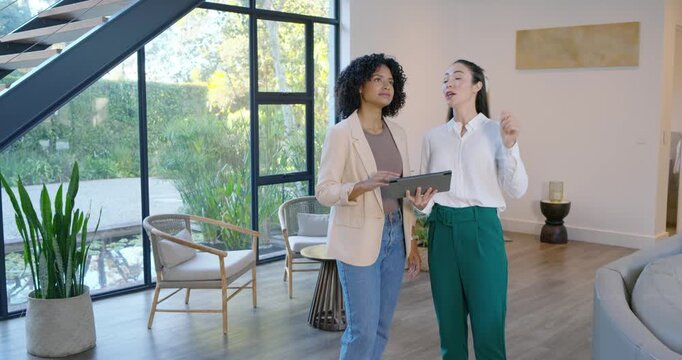 Diverse female colleagues consulting tablet in living room after spotting ceiling feature, pointing