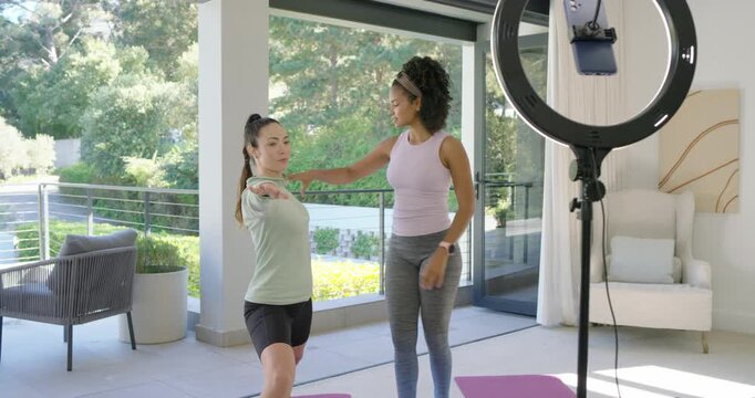 Female trainer guiding client assuming lunge on patio fixing form with pink band and ring light