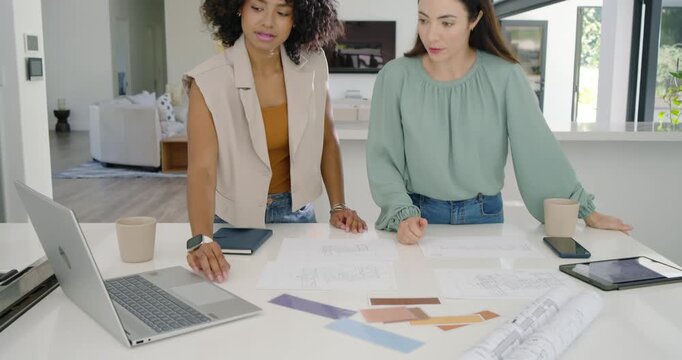 Diverse women coworkers seeing printed plan leaning at home table unrolling plans finalizing design
