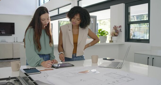 Diverse female colleagues leaning over kitchen island checking plans tapping tablet planning layout