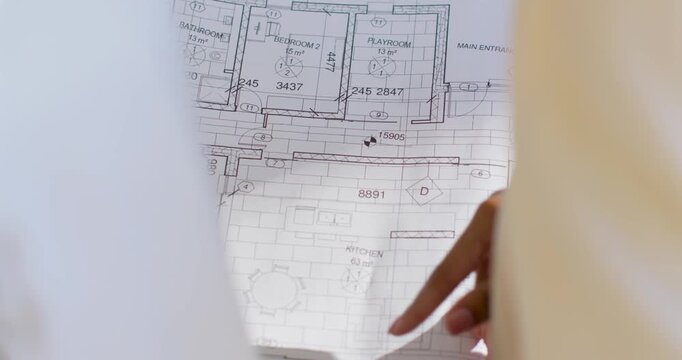 Right hand entering and smoothing floor plan at desk pointing playroom or main entrance reviewing pl