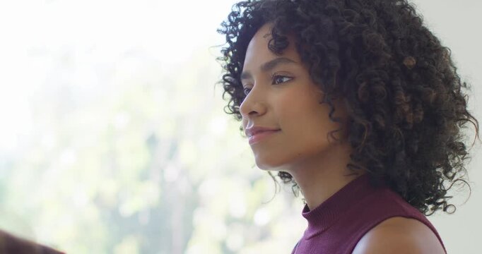Woman listening and smiling at off-frame speaker by window in maroon top, copy space