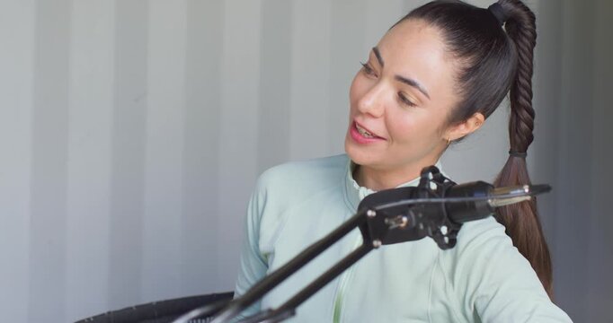 Adult female in zip-top after offscreen cue adjusting ponytail and speaking into mic in studio