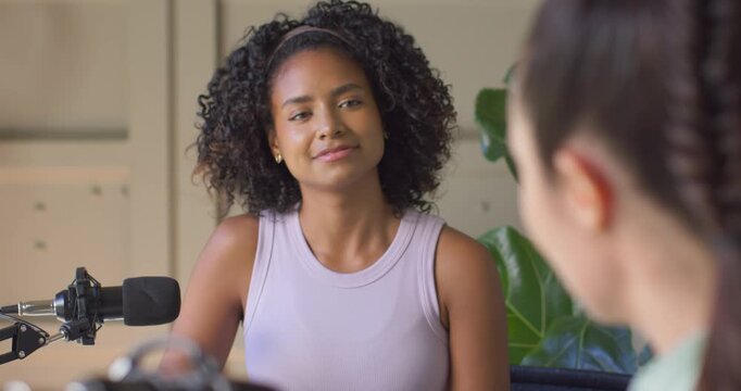 African American woman listening to blurred host speaking, then speaking into mic for home podcast