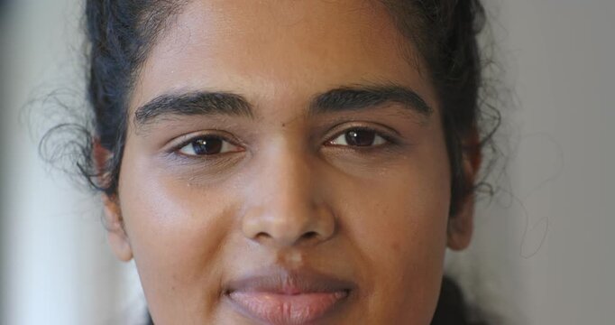 Adult female with braided hair opening eyes, shifting from neutral face to toothy smile in studio