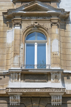 The weathered facade of an old building in Zagreb features an arched window with decorative stone carvings, pilasters and a classic triangular pediment