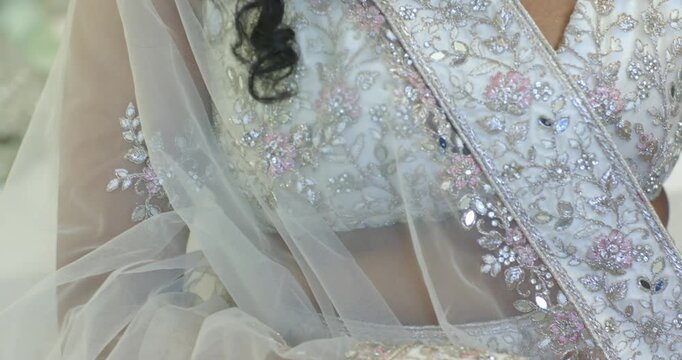 Female adjusting beaded sash and sheer dupatta in lounge, smoothing pleats, preparing for event