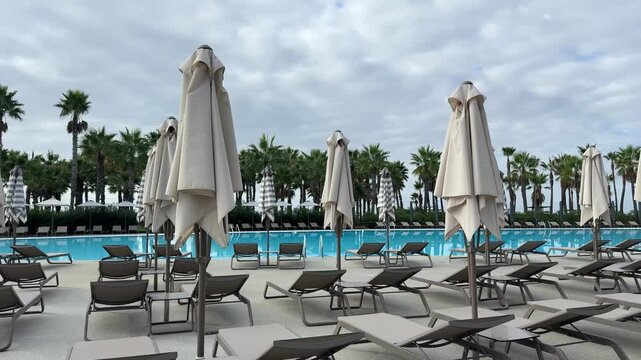 Sun loungers and closed umbrellas by resort pool on cloudy day