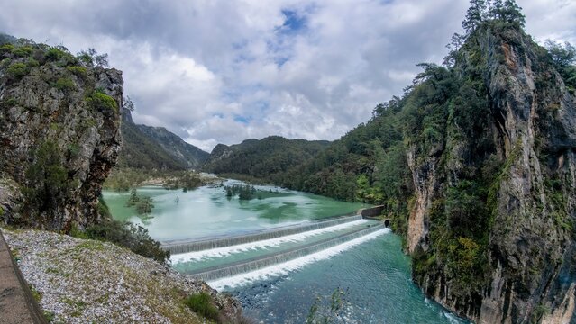 Turquoise waters of the Namnam River cascade over a stepped weir between moss covered rocky cliffs and dense pine forest in Mugla, Turkey