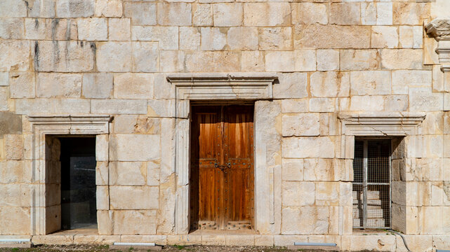 Ancient limestone facade with a locked wooden double door and framed window niches at the Patara archaeological site, Antalya, Turkey