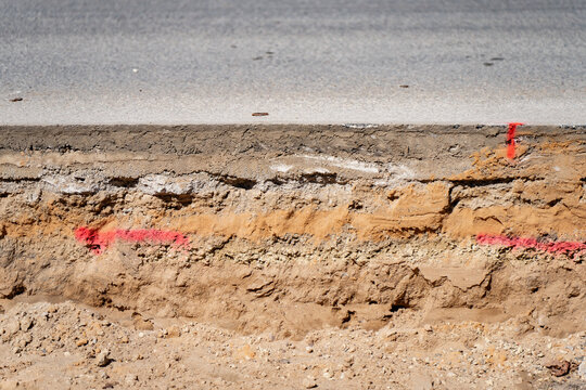 Cross section of asphalt road layers showing concrete base and sandy soil subgrade with red spray paint markings for civil engineering and urban infrastructure repair