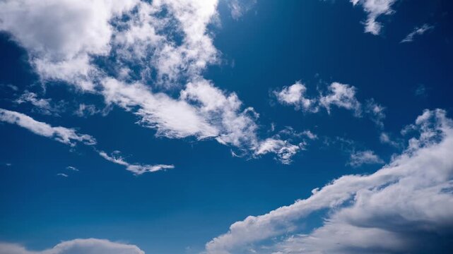 Various white cloud types including cumulus and wispy cirrus drift and evolve across a bright blue sky. Sunlight illuminates the dynamic atmospheric scene and vapors.