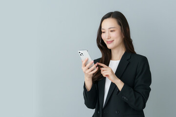 Fototapeta premium グレーバックのスマホを持つ若いスーツの日本人女性