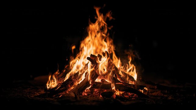 Campfire close up with warm orange flames and glowing embers on pure black background