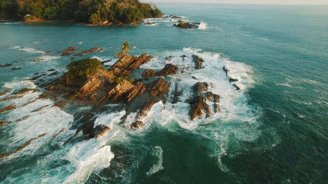 Golden light over rocky island with ocean waves breaking at Dominicalito beach Costa Rica