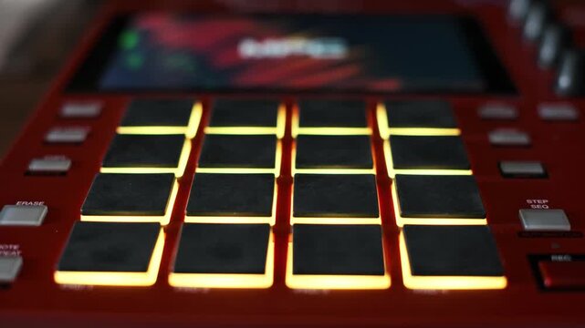 A close-up view focuses on the rubber pads of a red electronic beat maker illuminating with changing LED colors. Concept of electronic music production, rhythm sequencing, and studio gear.