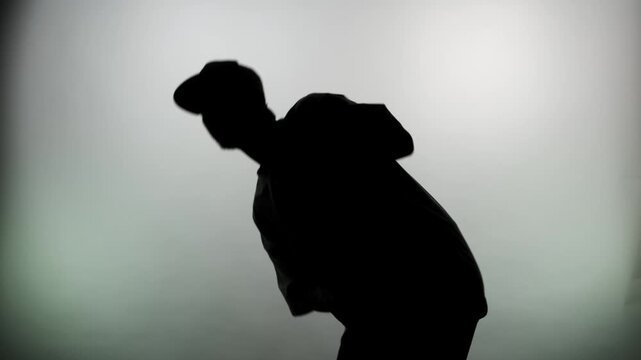 An anonymous silhouette of a man in a cap against a white wall, waving his legs in different directions