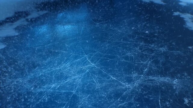 Slow motion top down tracking shot of ice rink surface showing skate scratches grooves and falling snow particles in indoor arena