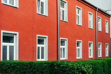 Prostejov, Czech Republic - April 18, 2026: Red orange townhouse wall with repeating white framed windows and trimmed hedge, ulice Újezd © Professional Art