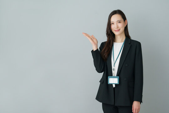 グレーバックの手のひらを広げるポーズをする若いスーツの日本人女性