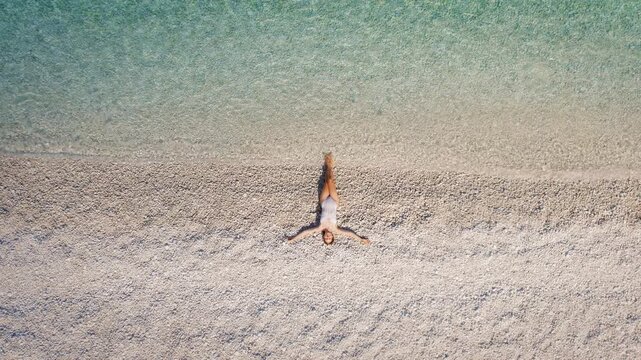 Woman relaxing on a pebble beach by the crystal clear sea in Kefalonia Greece