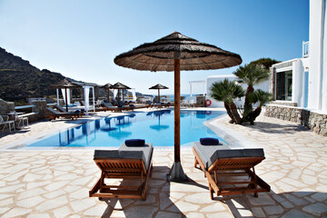 Luxury swimming pool with sunbeds and parasol in a Mediterranean resort setting. Bright summer scene with blue sky, clear water and relaxing atmosphere,. © Nikos