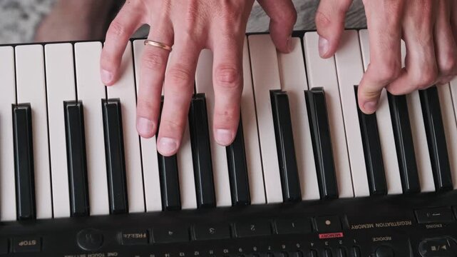 Top-down view of a composer hands playing chords on the keys of a synthesizer. This overhead shot captures the artist fingers pressing the keyboard during a musical performance or lesson.
