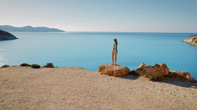 Woman standing on a rock overlooking turquoise Mediterranean sea in Kefalonia