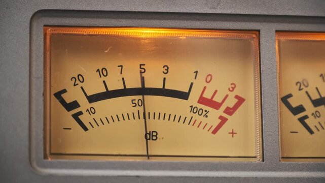 A macro lens captures the analog volume unit meter on a retro audio device. The fluctuating needle indicates sound levels against a warm yellow backlight.