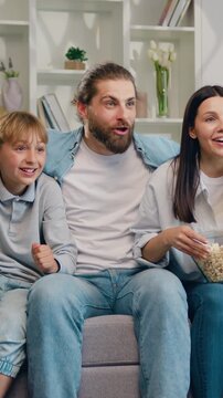 Happy parents, woman, man and children with ball, supporting the victory of their favorite football team. Family sitting on sofa at home watching live broadcasting of football game together