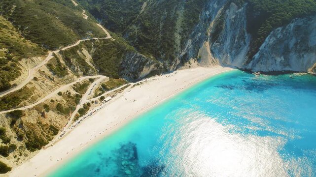 Breathtaking aerial view of a bright turquoise beach and curving road in Kefalonia Greece