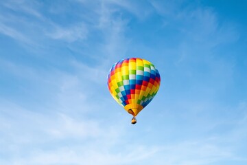 Fototapeta premium Colorful Hot Air Balloon Flies Across a Blue Sky With Wispy Clouds During a Sunny Day