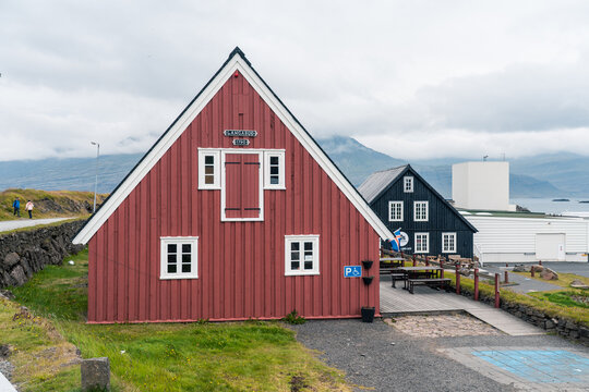 View of the historic Langabud red wooden house with its steep gabled roof and white-trimmed windows under a cloudy sky in Djupivogur, Mulathing, Iceland.