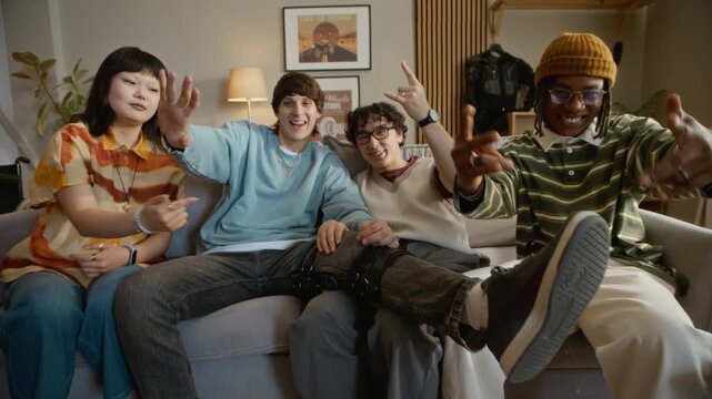 Push in shot of biracial young adult friends resting on comfortable sofa together and posing for camera