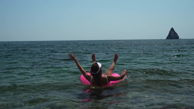 Woman, Sea, Inflatable ring. Happy female in white swimsuit and sunglasses splashes, having fun with pink float in clear blue ocean on sunny summer day.