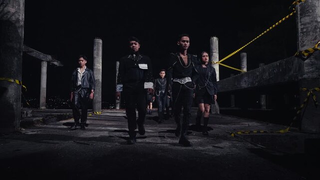 A crew of stylish models in edgy black outfits walks with attitude towards the camera through an unfinished building at night. A powerful, confrontational shot for fashion or music concepts.