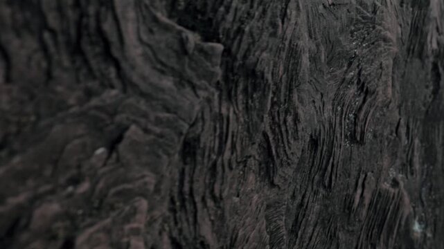 Extreme close-up of dark, rugged stone texture of an ancient kurgan in Khakassia. Handheld shot captures deep ridges, weathered surface, and megalith details with shallow depth of field.