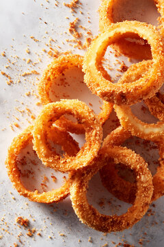 Crispy onion rings arranged with messy crumbs around on light background.