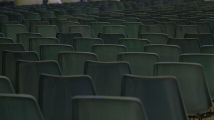 Fototapeta premium Dense rows of empty green plastic chairs closely arranged in symmetrical pattern inside large hall prepared for public gathering or conference