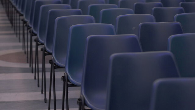 Symmetrical rows of empty blue chairs aligned on patterned floor inside expansive indoor venue prepared for public gathering or conference