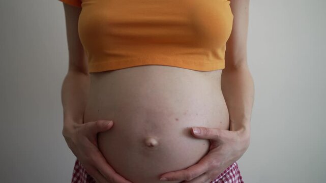Young expecting mother showing her pregnancy progress by dancing and affectionately caressing her belly, feeling the unborn baby kicking inside, a beautiful celebration of new life