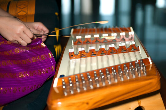 Close-up of a musician's hands playing a traditional Thai wooden dulcimer, known as a Khim, with small bamboo mallets.