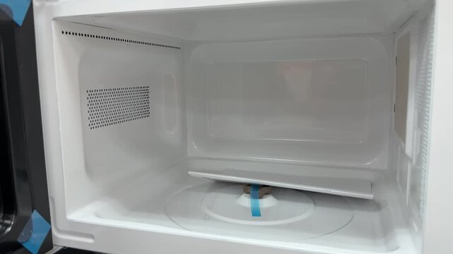 Open new microwave oven interior showing pristine white enamel cavity, glass turntable, black door frame with mesh, protective