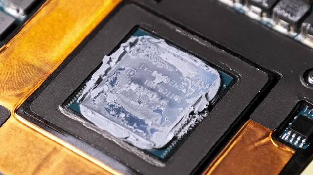A macro shot zooms out from a computer processor core with applied thermal grease. The view reveals electronic components and copper elements on the motherboard during repair.