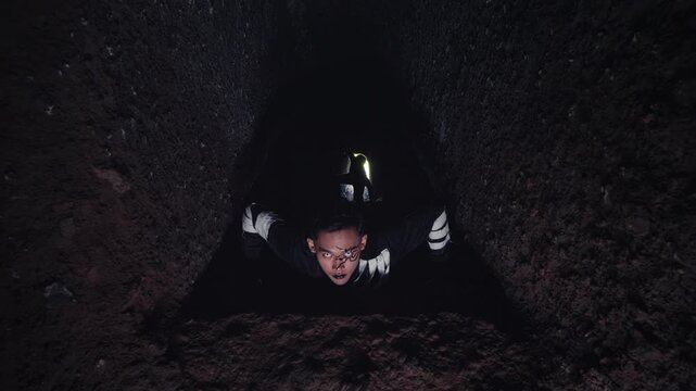 A high-angle view of a terrified man with dramatic face paint staring up from the bottom of a dark pit. His intense, crazed expression evokes horror, fear, and the feeling of being trapped.